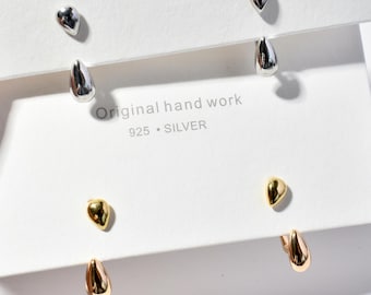 May include: A collection of silver and gold-toned teardrop earrings. The earrings are displayed on a white card with the text "Original hand work 925 SILVER". The earrings have a smooth, polished finish and a simple, elegant design.
