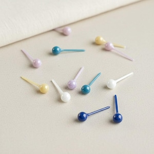 Op de afbeelding: Een verzameling kleine, kleurrijke, lepelvormige objecten verspreid op een neutrale ondergrond. De lepels hebben een afgeronde kop en een dun handvat, met kleuren als blauw, wit, geel en paars. De objecten lijken decoratief of voor knutselwerk.