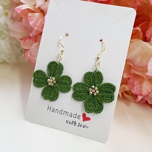 Pode incluir: Brincos de flores de crochê verde com contas douradas no centro. Os brincos estão pendurados em ganchos dourados em um cartão branco com o texto "Handmade with love".