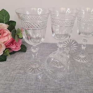 May include: Four clear glass wine glasses with a diamond pattern on the bowl and stem. The glasses are on a gray textured surface.