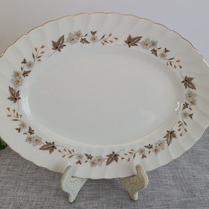 May include: A white oval serving platter with a gold rim and a floral design in shades of brown and green.