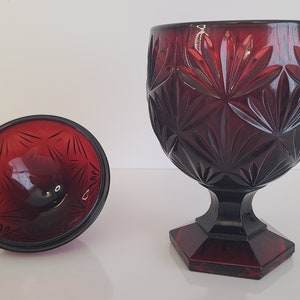 May include: A red glass candy dish with a footed base and a lid. The dish has a geometric pattern.