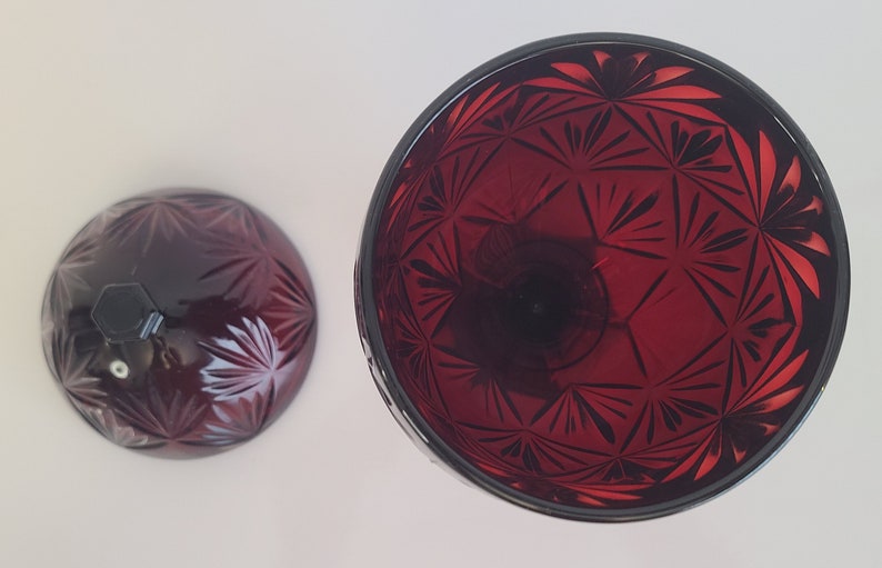 May include: A set of two red glass candle holders with a geometric pattern. The candle holders are made of clear glass with a red tint and have a starburst pattern.