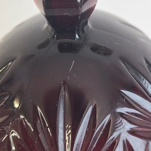 May include: A dark red glass cloche with a faceted design. The cloche has a knob on top.
