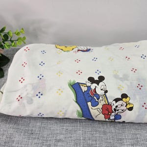May include: White sheet with a repeating pattern of red, blue, and yellow dots. The sheet features a colorful illustration of Mickey and Minnie Mouse. The sheet is folded and resting on a gray surface.