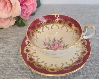 May include: A vintage teacup and saucer set with a red and gold floral design. The cup has a white interior with a pink rose and floral pattern. The saucer has a matching design.