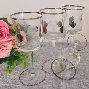 May include: Set of three clear glass wine glasses with silver rims. Each glass features an etched rose design.
