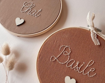 Puede incluir: Dos tapices bordados en aros de madera. Uno es de color canela con "Petit Chat" bordado en blanco, el otro es marrón con "Basile" bordado en blanco. Cada uno tiene un pequeño corazón de madera y una cinta de encaje.