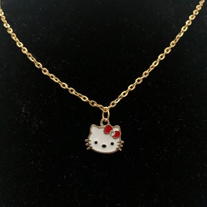 Peut inclure: Un collier en chaîne dorée avec un pendentif Hello Kitty blanc avec un nœud rouge et un seul strass.