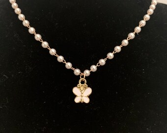 May include: A delicate pearl necklace with a small gold butterfly pendant. The butterfly has white enamel wings.