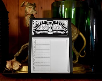 May include: Black and white notepad with a decorative top featuring an hourglass, wings, and the words "Fugit Hora." The notepad has a checklist and a blank section. A brass dog statue is in the background.