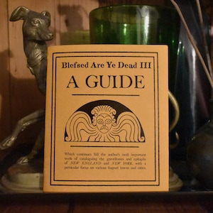 May include: A yellow guide book with the title "Blefsed Are Ye Dead III A GUIDE" and a black and white illustration of a winged creature with a human face. The text below the illustration reads "Which continues till the author's most important work of cataloguing the gravestones and epitaphs of NEW ENGLAND and NEW YORK, with a particular focus on various seaport towns and cities."