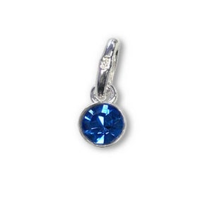 May include: A small, round, blue gemstone charm with a silver-colored bail. The charm has a faceted, sapphire-like appearance, and is suspended from a simple, polished metal loop. The background is plain white.