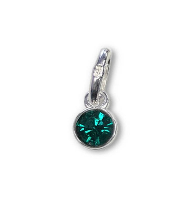 May include: A small, round, emerald green gemstone pendant with a silver-colored bail. The gemstone is set in a silver bezel and has multiple facets. The bail has a small, clear accent stone. This pendant is suitable for necklaces or bracelets.