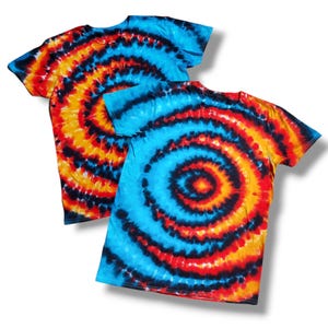 Könnte beinhalten: Zwei Batik-T-Shirts mit einem blauen, orangefarbenen und schwarzen Spiralmuster.
