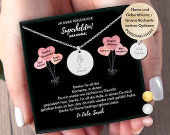 May include: A silver necklace with a round pendant that says "Sarah" and features a pink watercolour flower design. The pendant is attached to a chain with a small charm that says "Super Mama". The necklace is presented in a black box with a message that reads "An meine persönliche Superheldin! (AKA Mama)".