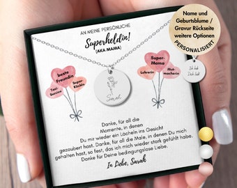 May include: A silver necklace with two round pendants. The larger pendant features a floral design and the name "Sarah" engraved on it. The smaller pendant has the words "Super Mama" on it. The necklace is presented in a black box with a white card that reads "An meine persönliche Superheldin! (AKA Mama)" and a message of appreciation.