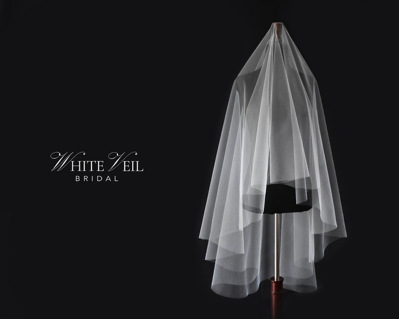 May include: A sheer white bridal veil draped over a mannequin, featuring multiple layers of soft tulle fabric. The text White Veil BRIDAL is printed in white on the left side against a solid black background, creating a clear visual contrast.