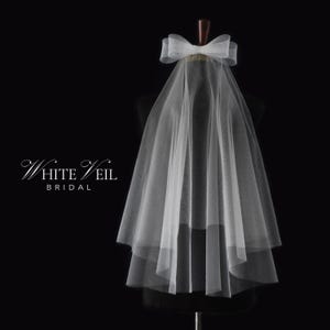 Könnte beinhalten: Ein weißer Braut Schleier mit einer großen weißen Schleife oben. Der Schleier ist aus weichem Tüll und hat eine einzige Schicht.