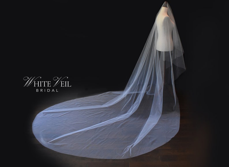 May include: A long, sheer white bridal veil draped over a mannequin, extending across the floor in a circular train. The text White Veil BRIDAL is printed in white on the left side against a dark background, showcasing the elegant, flowing fabric.