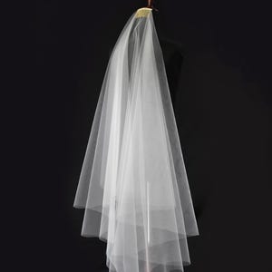 May include: A sheer white wedding veil made of fine tulle fabric, featuring multiple cascading layers that create a soft, voluminous silhouette. The veil is securely attached to a gold-toned metal comb, designed for easy placement in hair.