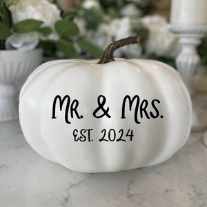 May include: White pumpkin with black lettering that reads "Mr. & Mrs. Est. 2024".