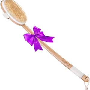 Puede incluir: Un cepillo de espalda de madera con cerdas naturales y un mango largo. El cabezal del cepillo es de forma ovalada y está unido a un mango de madera marrón claro. Un lazo morado está atado alrededor del mango. El mango tiene una envoltura blanca.