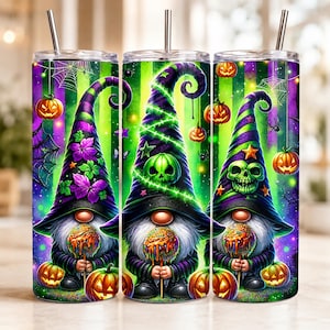 May include: A cylindrical tumbler with a metal straw featuring a vibrant Halloween design. The print displays three gnomes wearing tall, pointed hats in purple and green, decorated with skulls, pumpkins, spiderwebs, and colorful flowers.