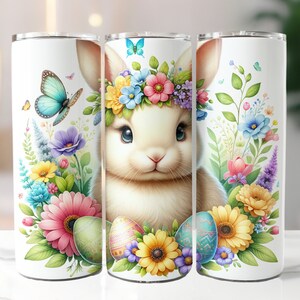 May include: Three white stainless steel tumblers with a colorful Easter bunny design. The bunny is wearing a flower crown and surrounded by flowers and Easter eggs.