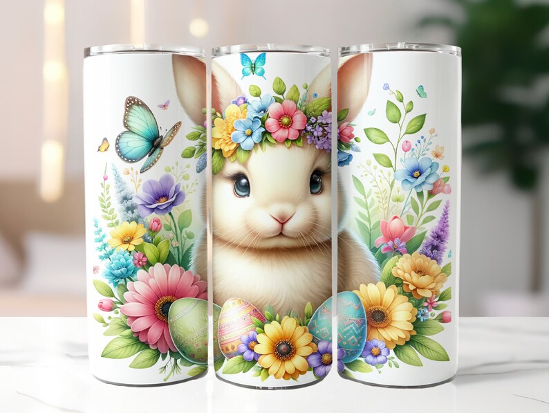 May include: Three white stainless steel tumblers with a colorful Easter bunny design. The bunny is wearing a flower crown and surrounded by flowers and Easter eggs.