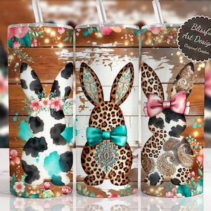 May include: Three stainless steel tumblers with bunny designs. Each tumbler features a different pattern: cow print, leopard print, and paisley. The tumblers have floral and turquoise accents, with a wooden background.