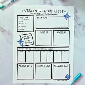 May include: A white paper with a black outline design for a weekly creative reset. The design includes sections for self-check-in, brain dump, must-do, and a weekly overview. The text includes "You're doing better than you think!" and "Done is better than perfect."