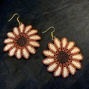 May include: A pair of brown and white crocheted sunflower earrings with gold hooks.