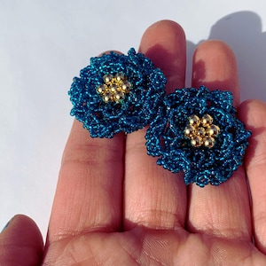 Puede incluir: Un par de pendientes de cuentas azul turquesa con forma de flores con centros de cuentas doradas.