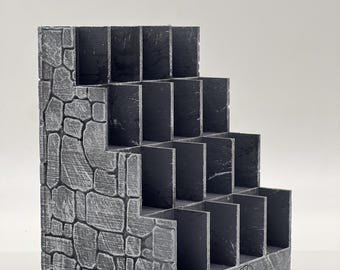 Può includere: Un espositore a gradini grigio con una texture a muro di pietra sui pannelli laterali. L'unità presenta diversi scomparti aperti disposti a scala. Il pannello frontale mostra il testo The SODA coaster in un carattere stilizzato.