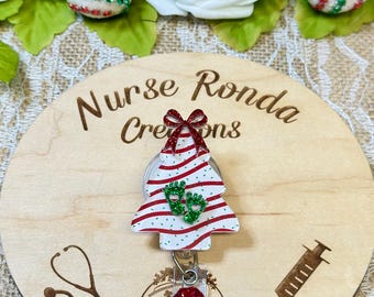May include: A wooden round badge holder with the text "Nurse Ronda Creations" engraved on it. A red and white striped Christmas tree with green glitter and a red bow is attached to the holder. A stethoscope and a syringe are also engraved on the holder.