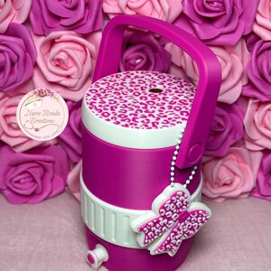 May include: A magenta water cooler with a white and leopard print lid and handle. A white and pink bow charm hangs from the handle. The cooler has a white band and a spigot. The background features pink and magenta roses.