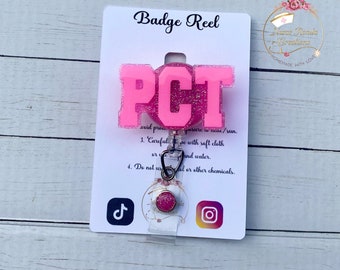 Könnte beinhalten: Rosaer Badge-Rollenhalter mit den Buchstaben "PCT" in Glitzer. Der Rollenhalter hat einen rosa Glitzer-Anhänger und eine transparente, einziehbare Schnur. Die Karte hinter dem Rollenhalter enthält Pflegehinweise und Social-Media-Symbole.