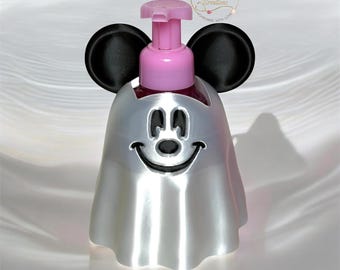 May include: A silver soap dispenser shaped like a ghost with a smiling face and black mouse ears. The top features a pink pump mechanism. A circular logo with the text Nurse Ronda Creations is visible in the upper right corner of the image.