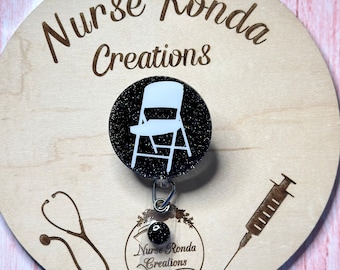 May include: Black and white glitter badge reel with a white chair silhouette on a black background. The reel has a clear plastic badge holder with a black and white floral design and the text "Nurse Ronda Creations" and "Homemade with Love".