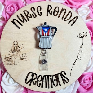 May include: A wooden badge reel with the text "Nurse Ronda Creations" and a drawing of a nurse. The reel features a silver coffee pot with the Puerto Rican flag. The words "registered nurse" are also on the reel.