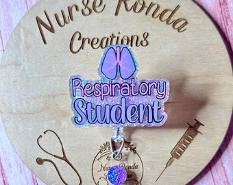 May include: A purple and pink glitter badge holder with a pink and white lung design and the text "Respiratory Student". The badge holder is attached to a retractable badge reel with a purple glitter charm.