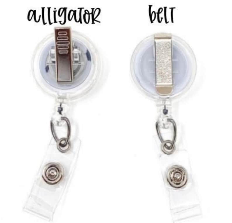 K&ouml;nnte beinhalten: Zwei ausziehbare Ausweishalter mit Alligatorclips und G&uuml;rtelclips. Die Ausweishalter sind aus klarem Kunststoff mit einem silbernen Metallclip.