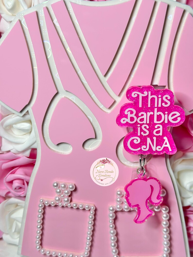 May include: Pink Barbie doll cutout with a pink and white dress and a pink charm that says "This Barbie is a CNA". The doll is holding a pink perfume bottle with a pearl trim.