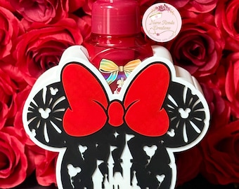 May include: A red soap dispenser sits in a white holder shaped like Minnie Mouse's head, with a large red bow and black silhouette details. The holder features a castle design. The background is a bed of red roses.