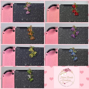 May include: A collection of Nintendo Switch consoles with pink Joy-Cons, each adorned with a floral charm in various colors. The charms feature detailed flower designs in shades of red, purple, orange, yellow, green, and blue, adding a decorative touch to the consoles.