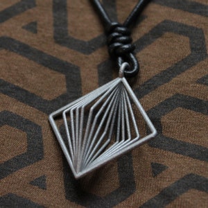 May include: A silver geometric pendant necklace with a black leather cord. The pendant is a square shape with a layered design.