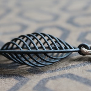 May include: A black metal leaf pendant with a delicate wire design. The pendant is attached to a brown leather cord.