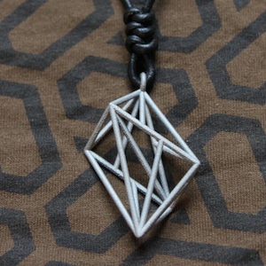 May include: A silver geometric pendant necklace with a black leather cord. The pendant is a three-dimensional shape with multiple intersecting lines.