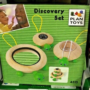 May include: A wooden toy set with three turtle-shaped pieces. The turtles have green shells and are decorated with a compass, a magnifying glass, and a ring. The box is green and white and says "Discovery Set" and "PLAN TOYS" in large letters. The product number is 4315.